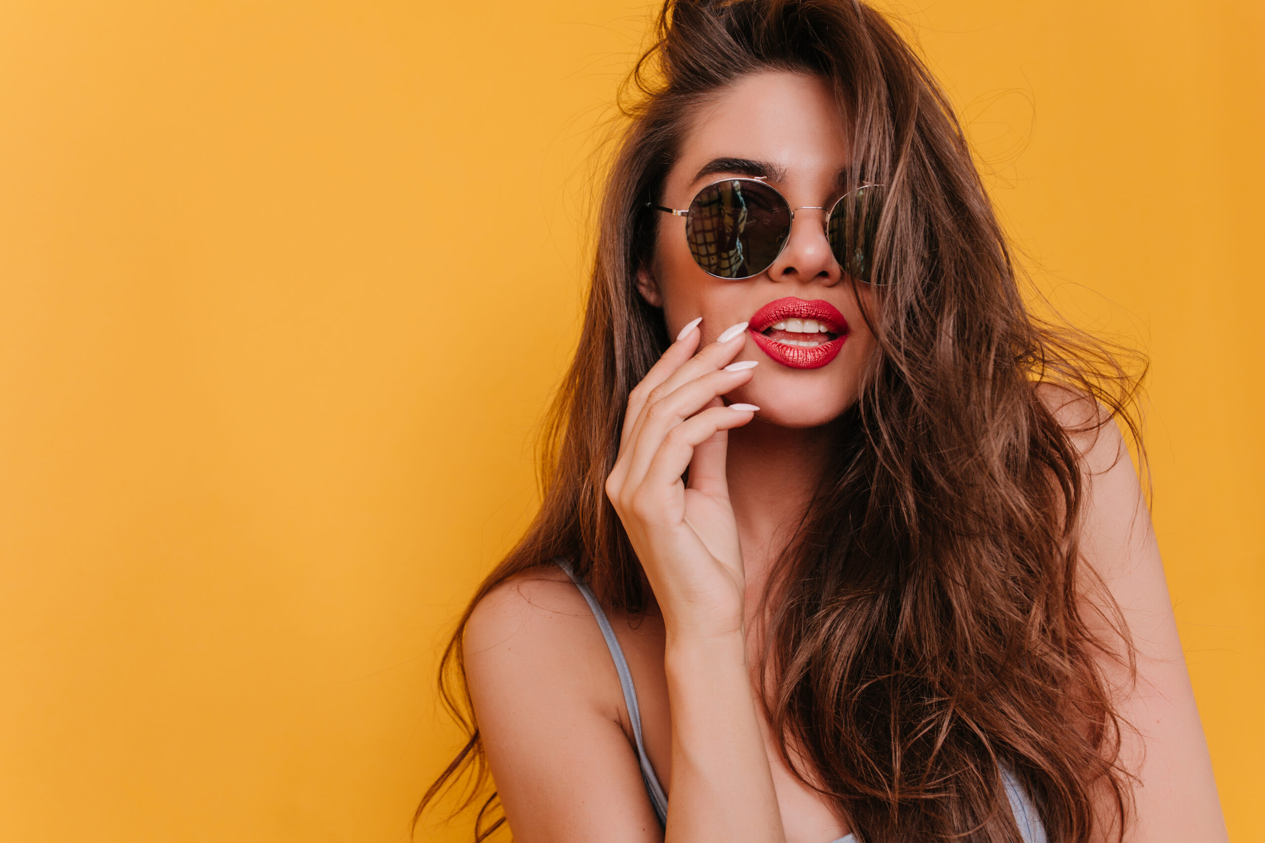 Close-up photo of beautiful white girl in black sunglasses. Studio shot of fascinating brunette lady isolated on bright yellow background.